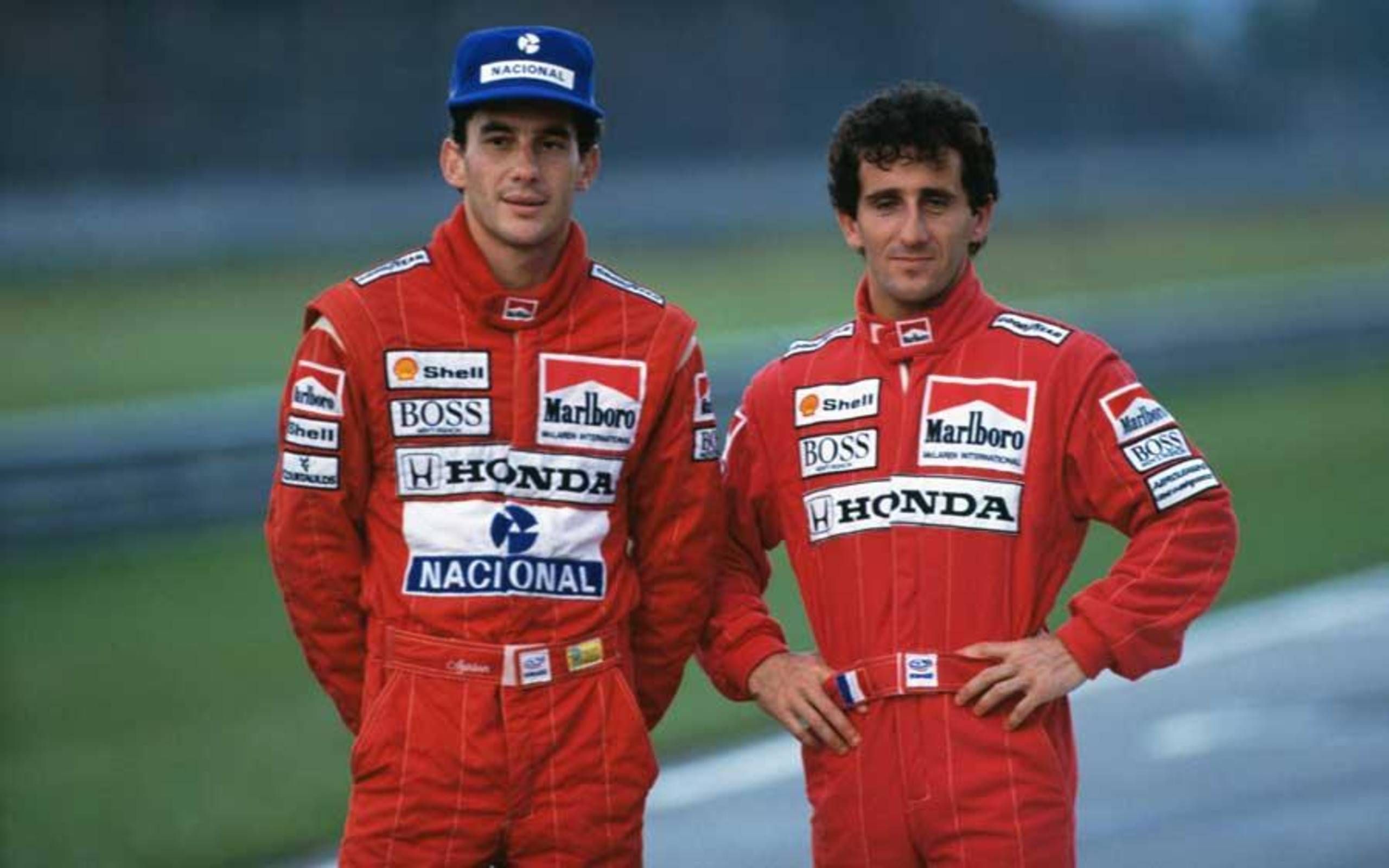Ayrton Senna e Alain Prost: Ayrton Senna e Alain Prost lado a lado, de macacão vermelho da McLaren-Honda, posando numa pista de corrida