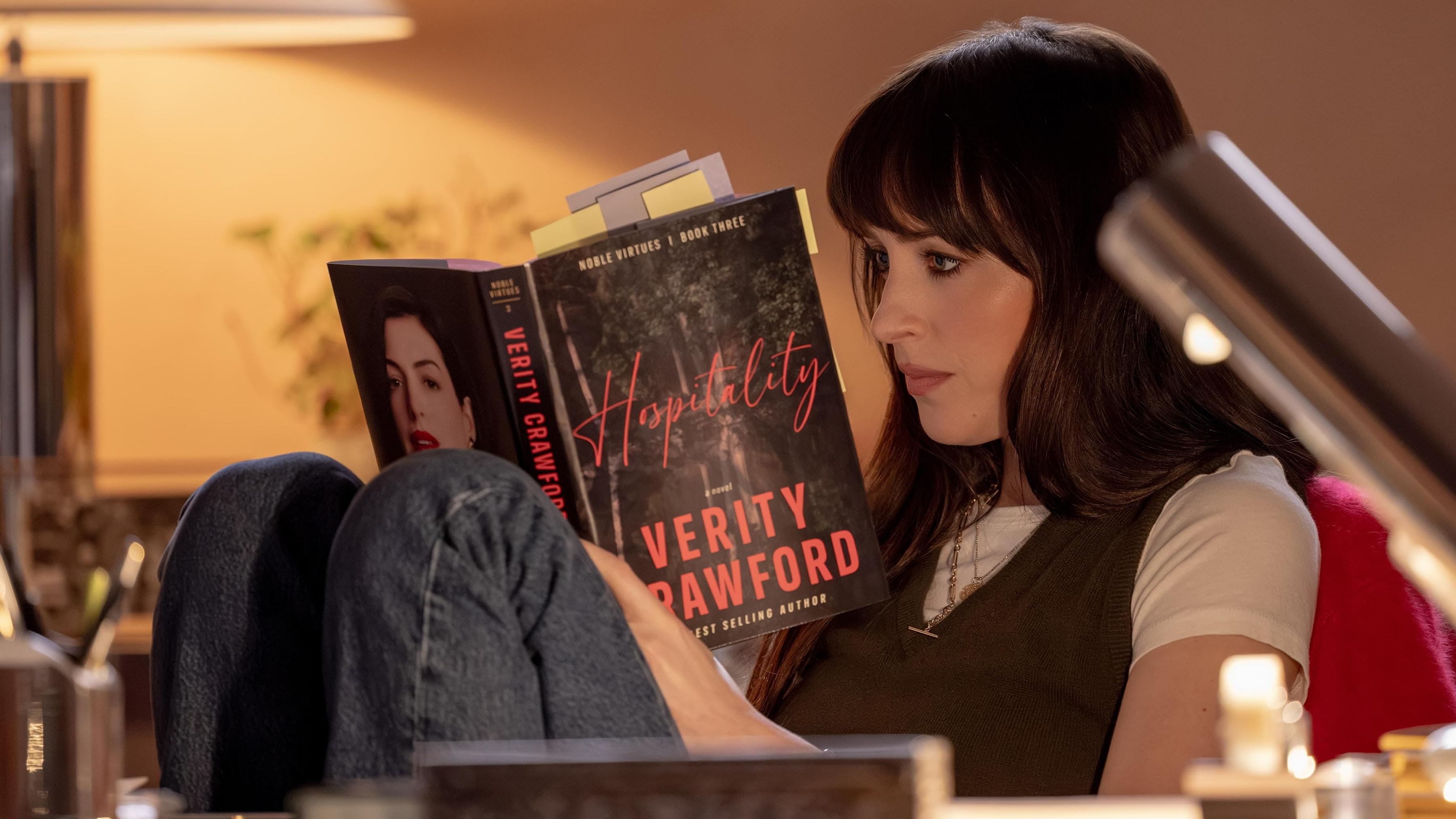 Lowen Ashleigh (Dakota Johnson) lê o livro "Hospitality", de Verity Crawford, enquanto está sentada em uma poltrona em cena do filme Verity.