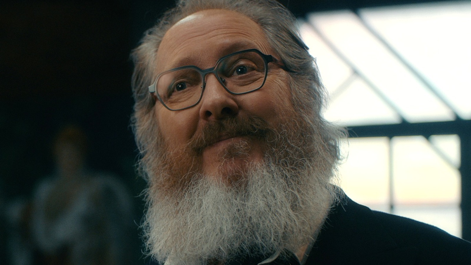 Close da versão humana do Ultron (James Spader), com barba grisalha e óculos, sorrindo, em cena de VisionQuest.