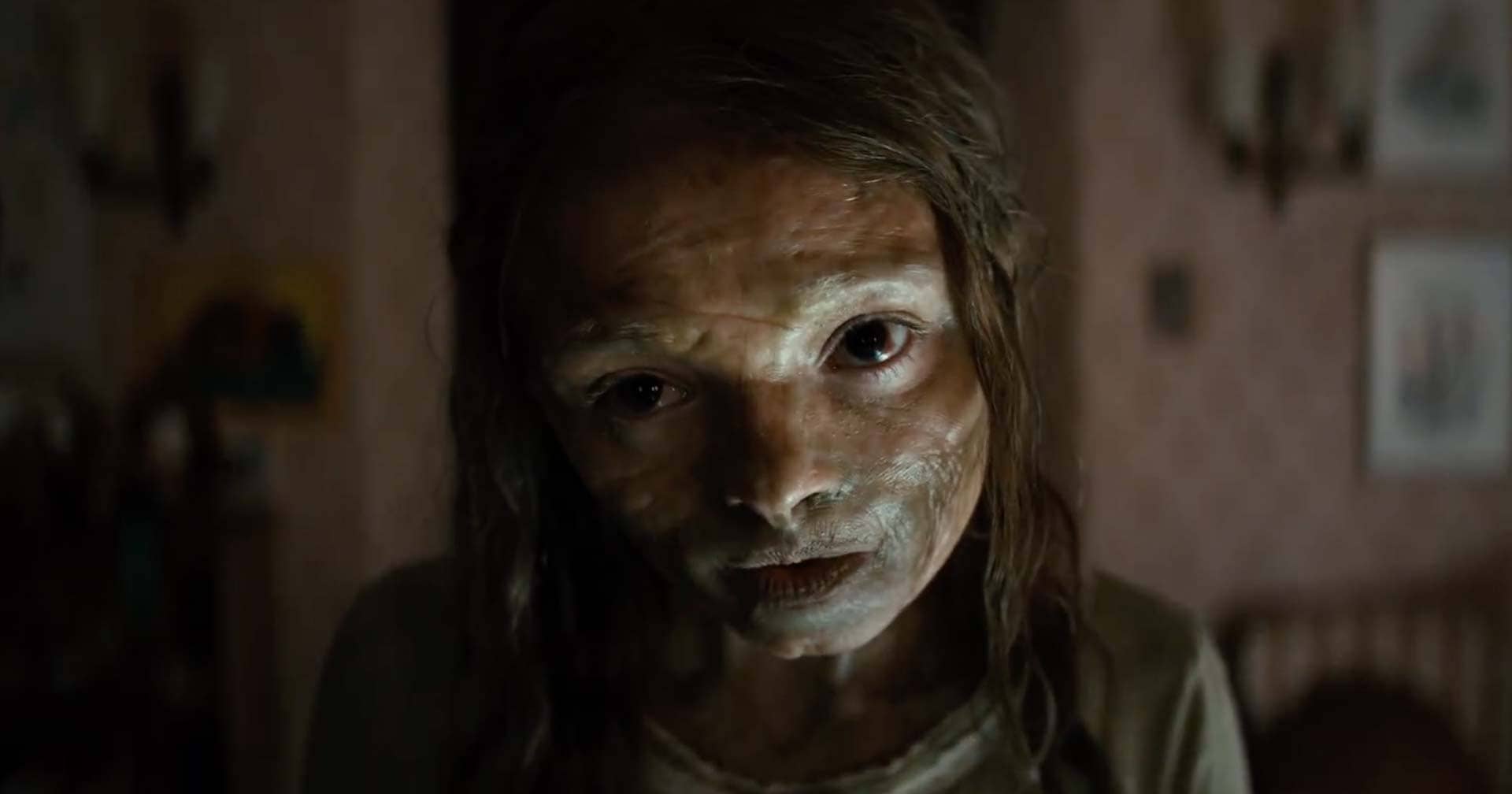 Katie Cannon (Natalie Grace) encara a câmera com o rosto meio mumificado em uma cena sombria do filme Maldição da Múmia.