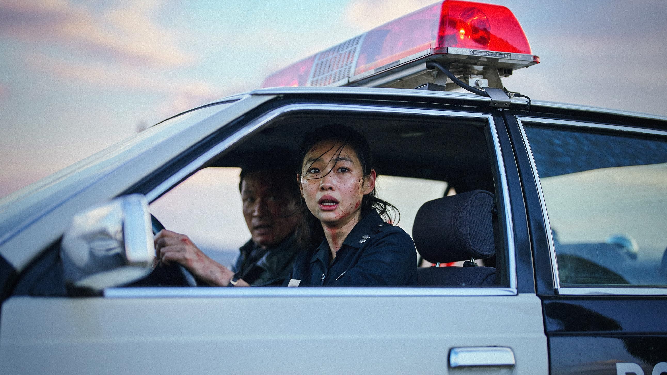 Sung-ae (Hoyeon), com o rosto sujo e machucado, no banco do motorista de uma viatura policial, enquanto Bum-seok (Hwang Jung-min) está no banco do passageiro. A policial olha pra frente com expressão chocada em uma cena do filme Hope: O Primeiro Impacto.