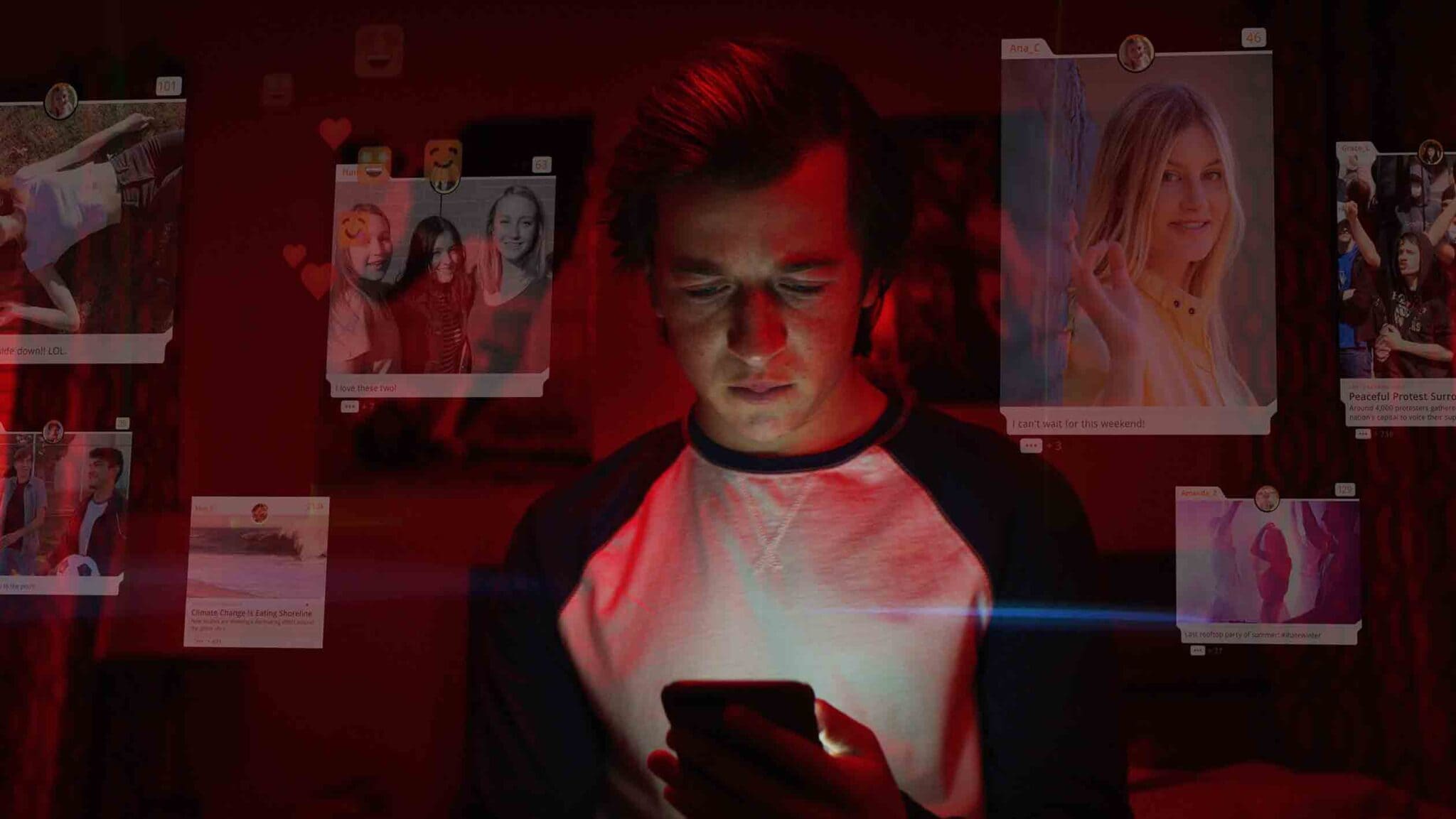 Cena do documentário O Dilema das Redes, com Ben (Skyler Gisondo) olhando pro celular em um ambiente escuro iluminado por luzes vermelhas, cercado por publicações e fotos de uma rede social projetadas ao seu redor.