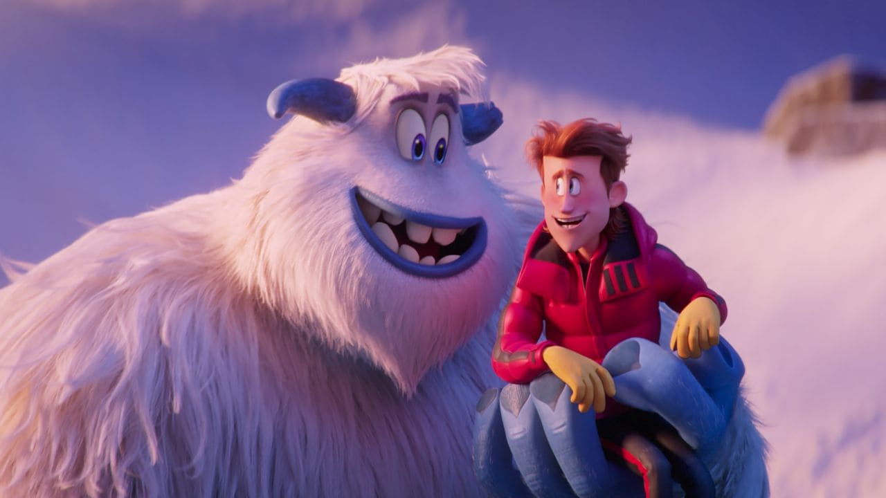 Migo (Channing Tatum), um yeti, com Percy Patterson (James Corden), um humano, em sua mão esquerda enquanto olham um pro outro e sorriem. Ao fundo vemos uma montanha nevada em cena do filme Pé Pequeno.