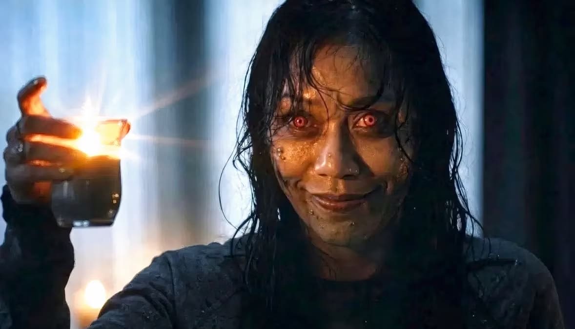 Thya (Luciane Buchanan) aparece com olhos amarelos, pele suja e expressão demoníaca, segurando um copo com uma vela em chamas em cena de A Morte do Demônio: Em Chamas.