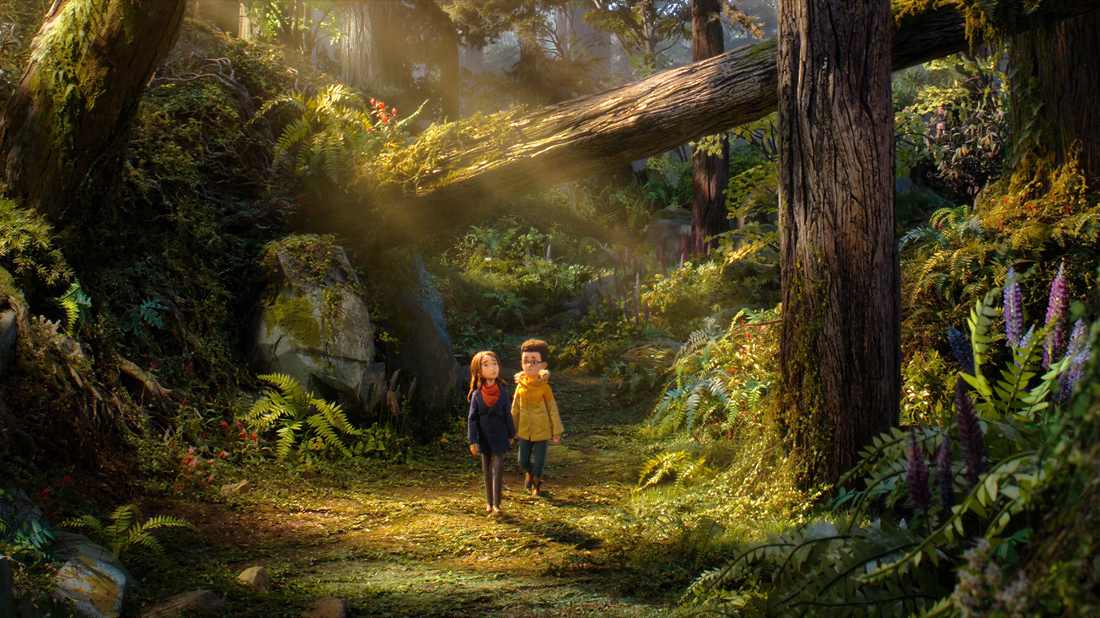 Prue McKeel (Peyton Elizabeth Lee) e Curtis Mehlberg (Jacob Tremblay) caminham pela floresta encantada em O Bosque Selvagem (Wildwood, 2026), cercados por árvores gigantes, vegetação exuberante e raios de sol.
